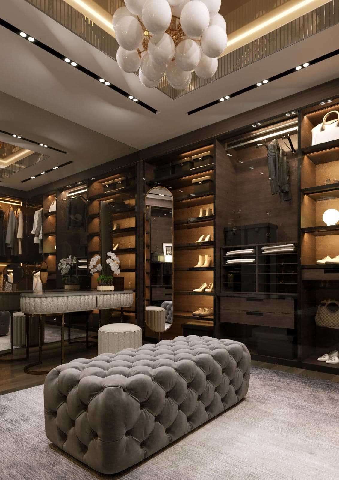 Luxurious walk-in closet with dark wood cabinetry, a grey tufted ottoman, and a bubble chandelier.