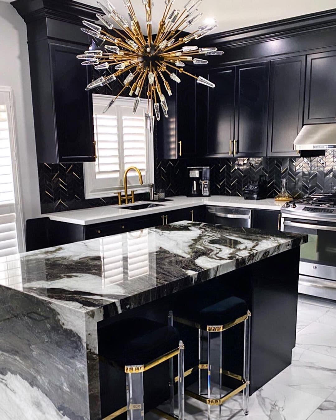 Luxurious kitchen with black cabinets, gold accents, a marble island, and a gold starburst chandelier.