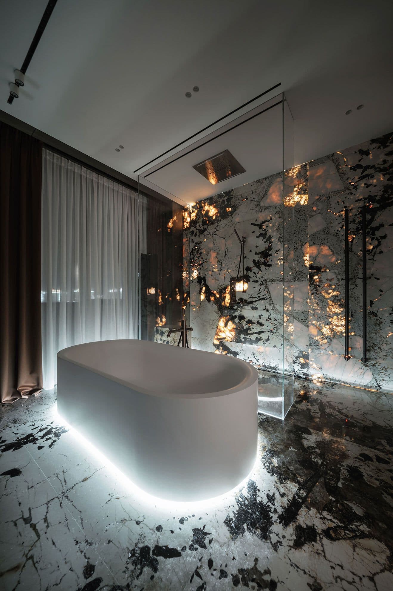 Modern bathroom featuring a glowing white bathtub and dramatic backlit black and white marble.