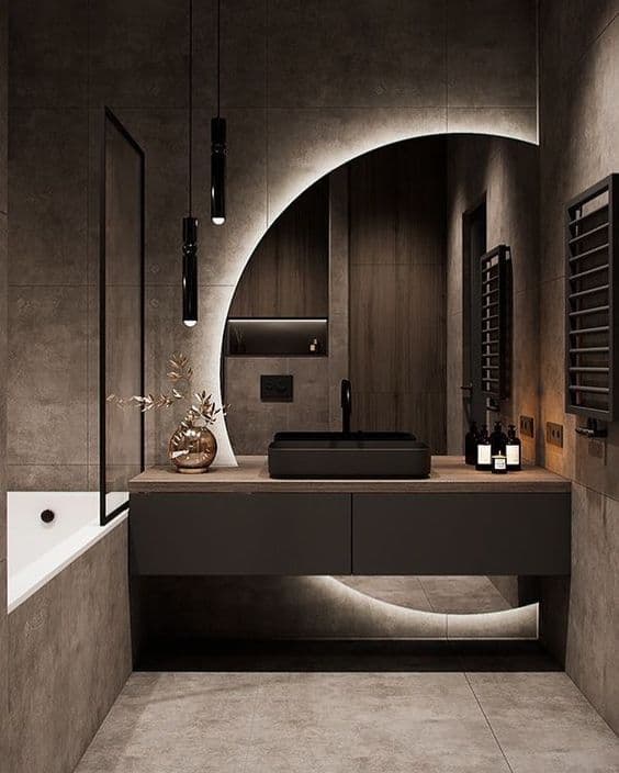 Modern dark bathroom featuring a backlit circular mirror, black vessel sink, and minimalist pendant lights.